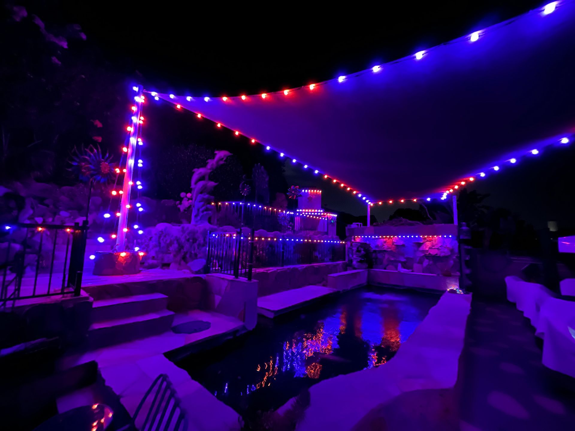 A swimming pool is lit up with purple and red lights at night.