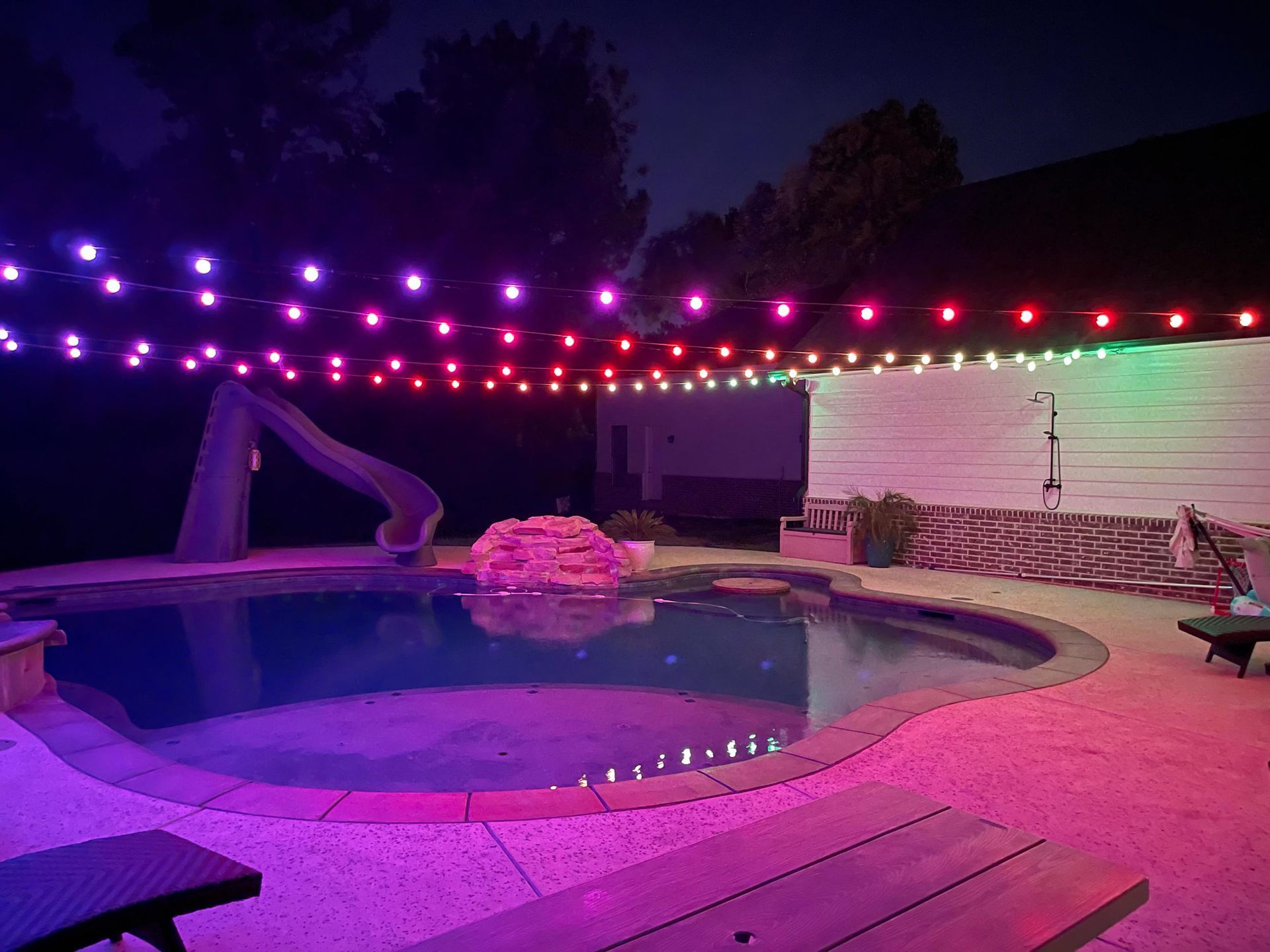 A swimming pool is lit up with purple and red lights at night.