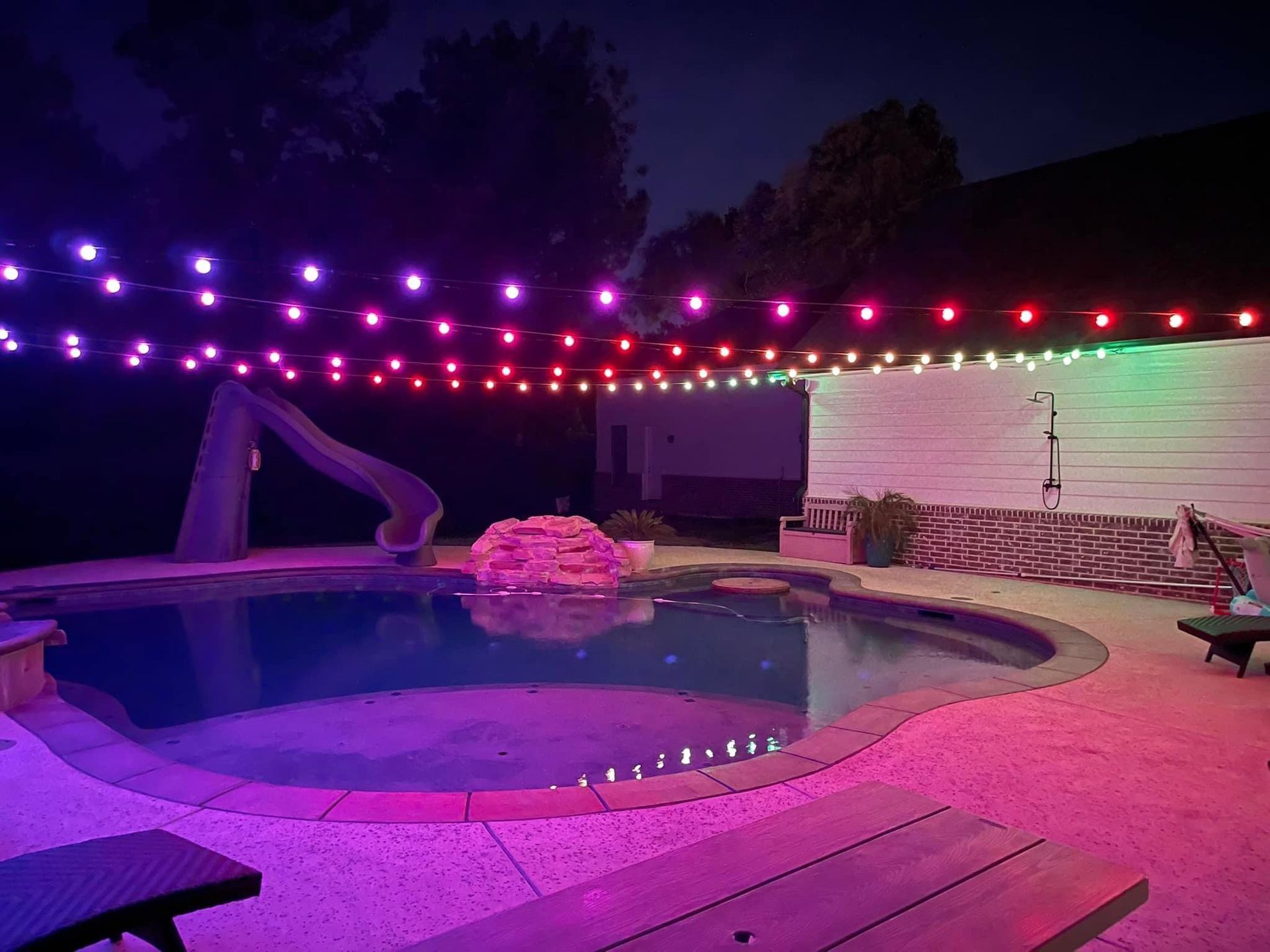 A swimming pool is lit up with christmas lights at night.