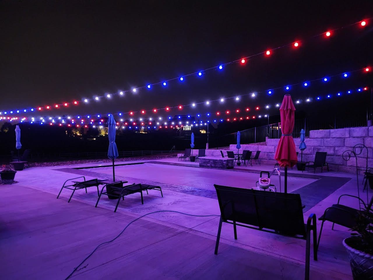 A swimming pool is lit up with red , white and blue lights at night.