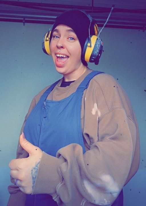 A woman wearing ear muffs is giving a thumbs up
