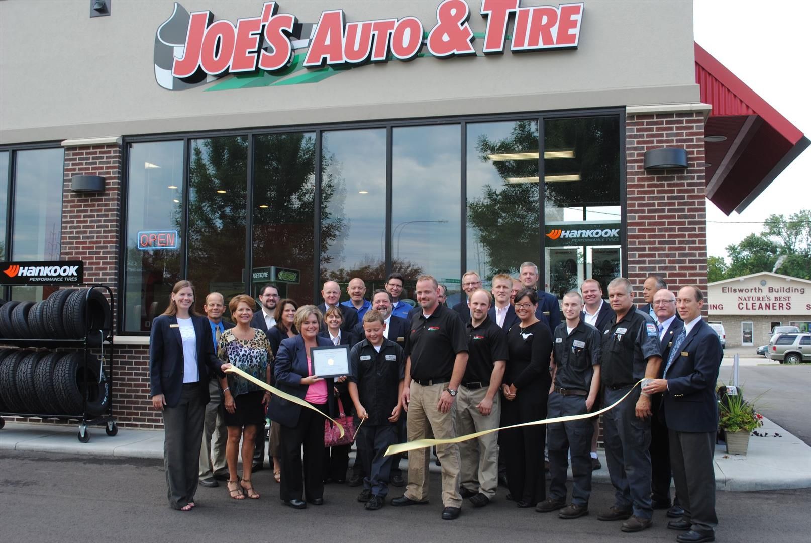 Group of people cutting a ribbon in front of Joe's Auto & Tire, celebrating a grand opening. | Joe's Auto and Tire