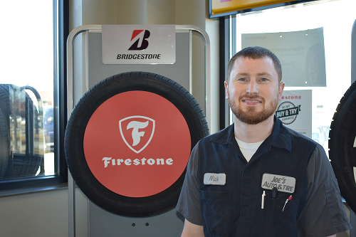 Man in a shop stands near a tire display with Firestone and Bridgestone logos. | Joe's Auto and Tire 