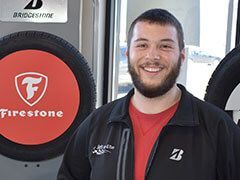 Man in black jacket smiles in front of a Firestone tire and Bridgestone sign. | Joe's Auto and Tire 