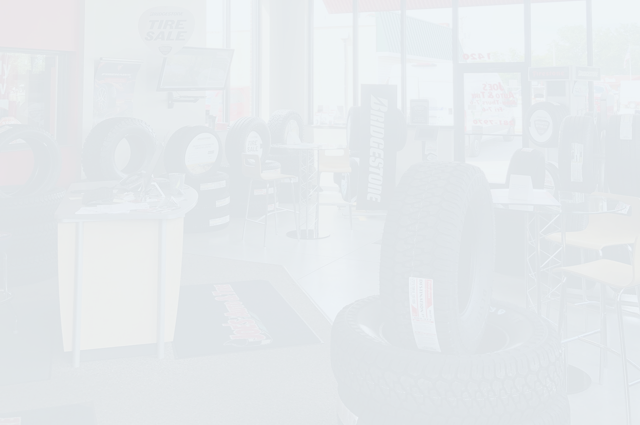 Tire shop interior with tires, a counter, and a blurry figure near a chair. | Joe's Auto and Tire