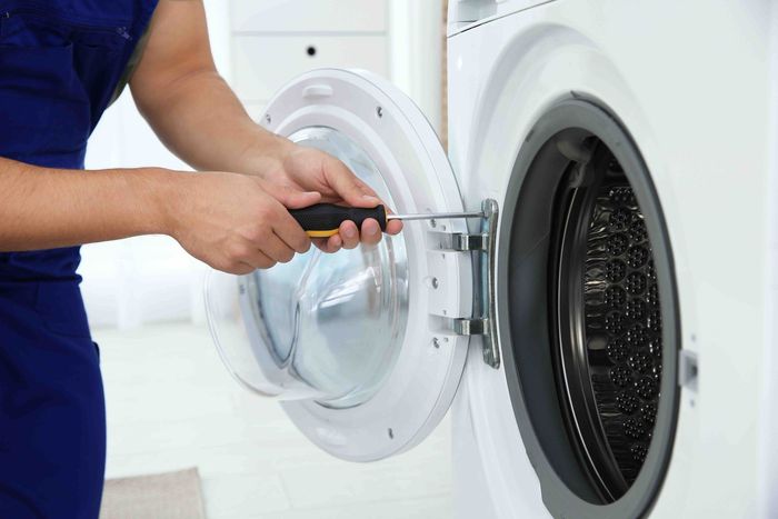 A man is fixing a washing machine with a screwdriver.