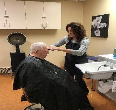 Elderly man receiving a haircut from a female hairdresser.