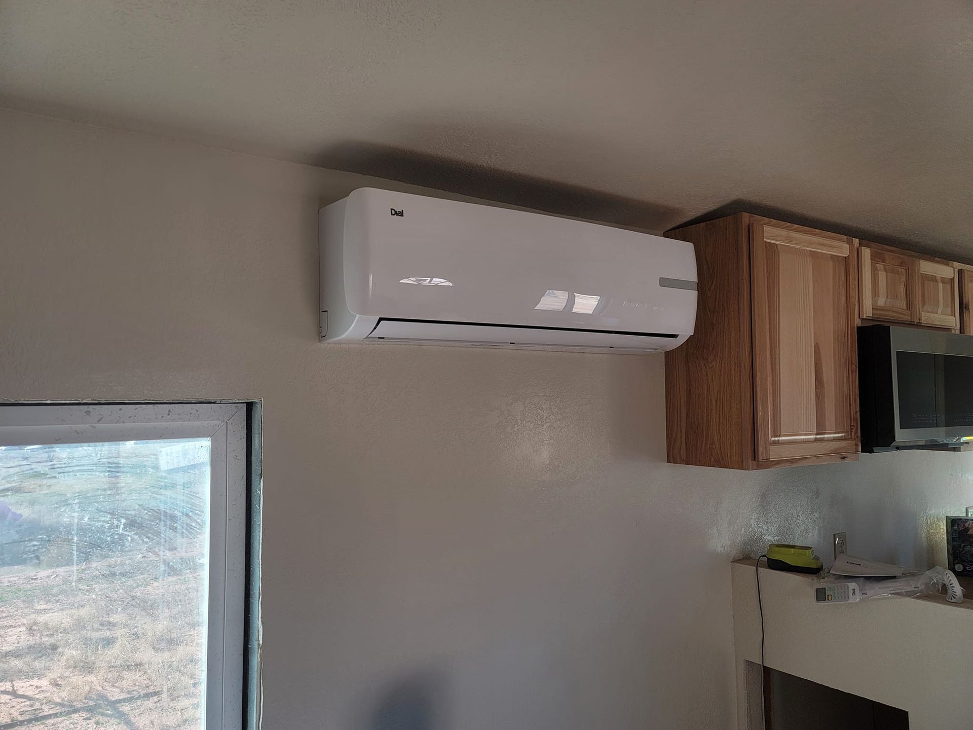 White wall-mounted air conditioner above cabinets and microwave, next to a window.