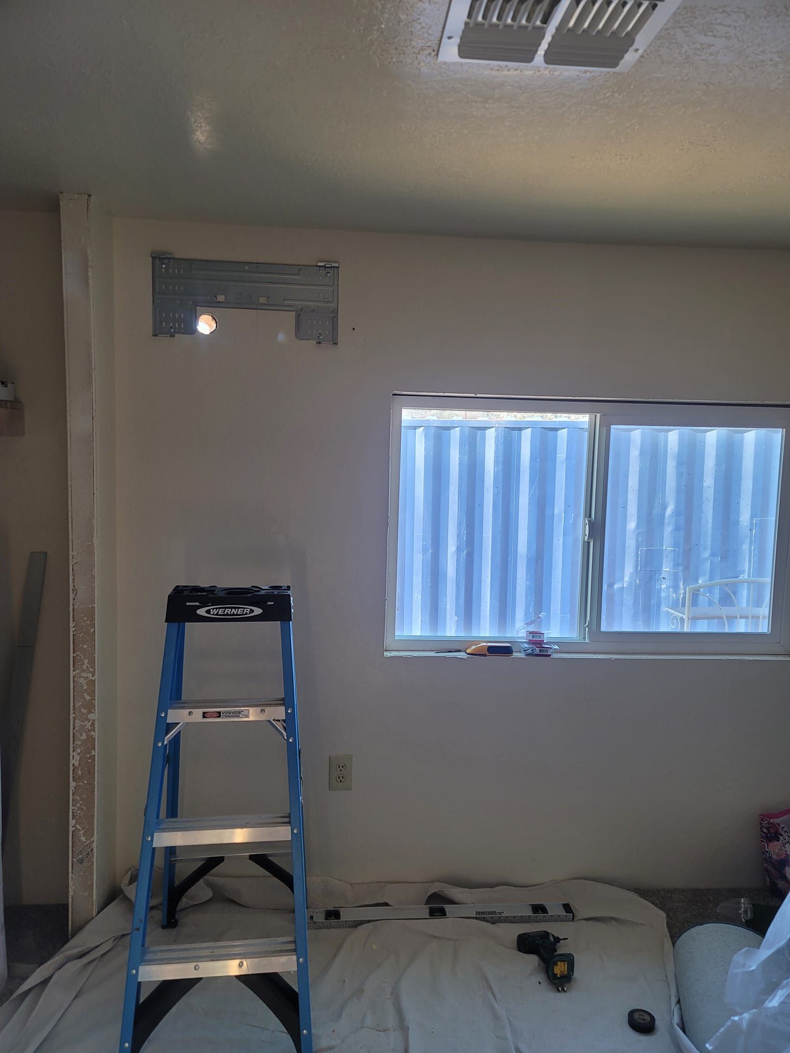 A room being renovated with a ladder, a window, and exposed wall sections.