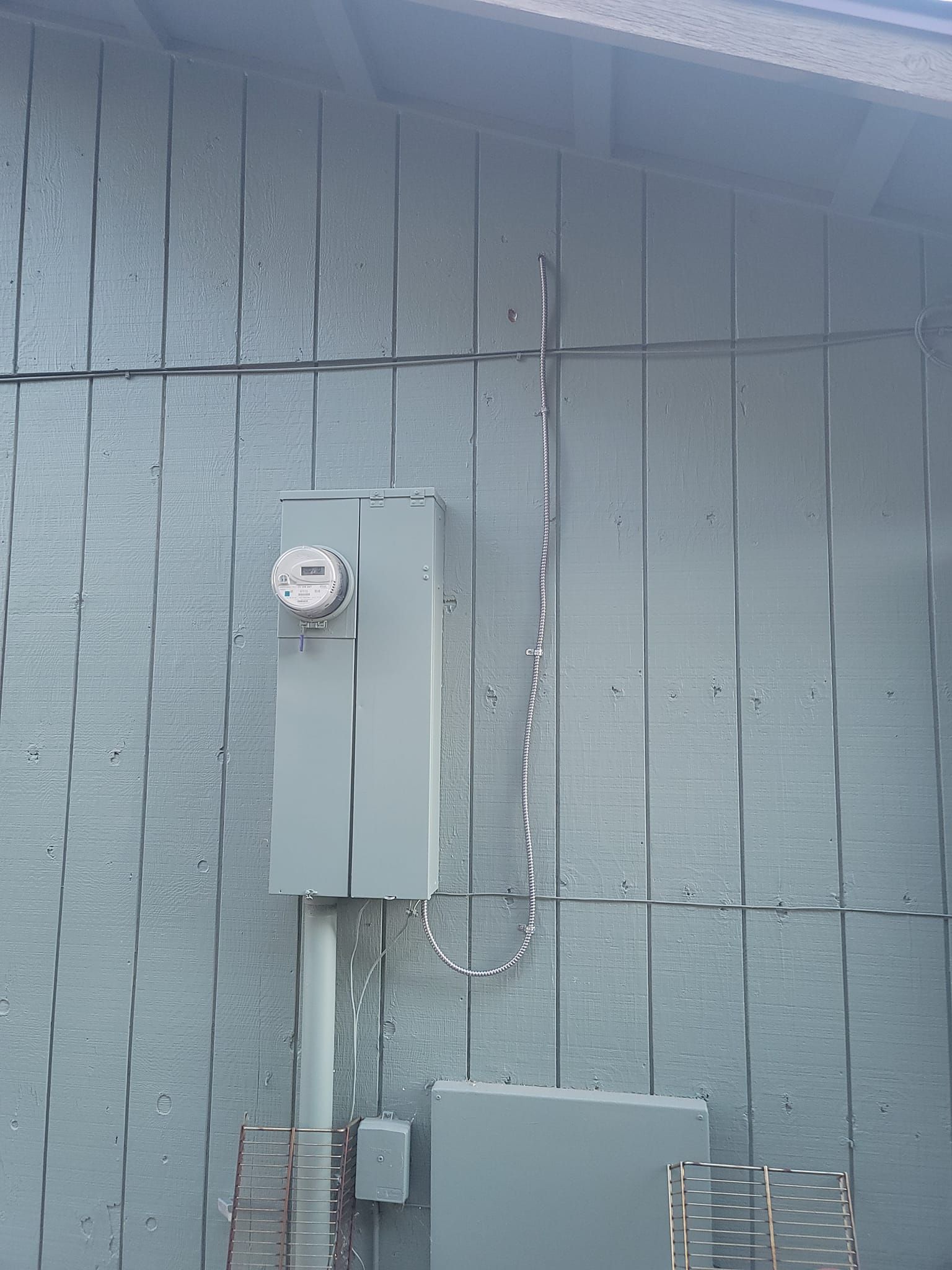 Gray electrical meter box and conduit mounted on a light blue painted wooden wall.