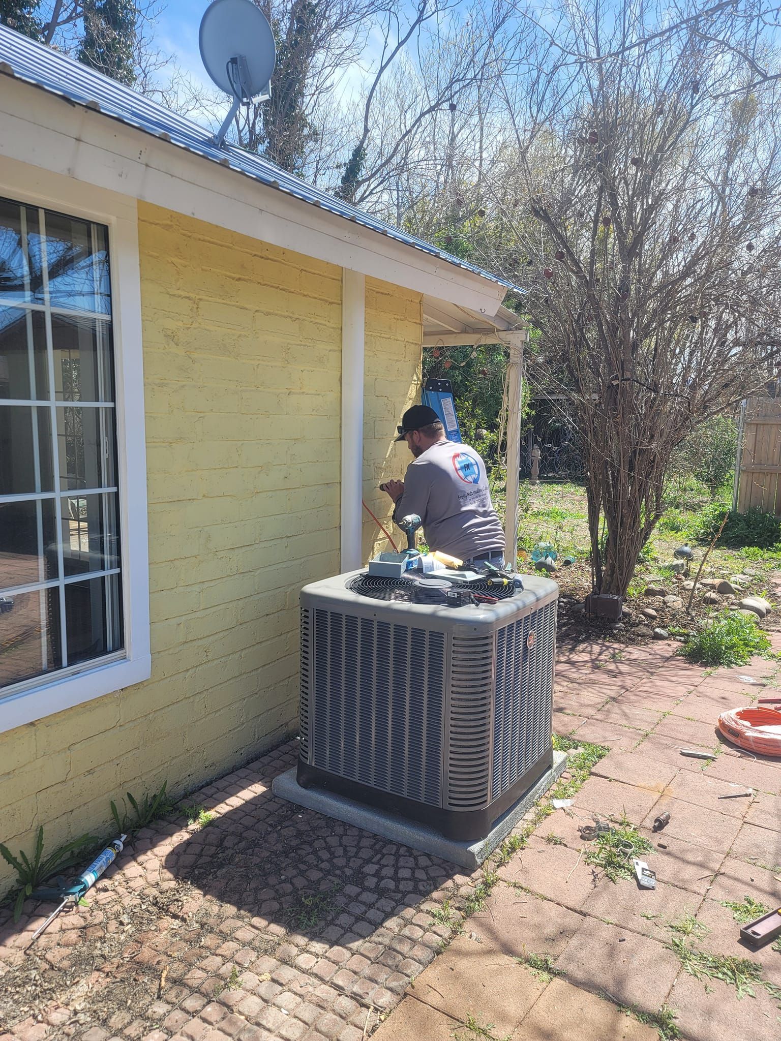 Person working on an air conditioning unit near a yellow building.
