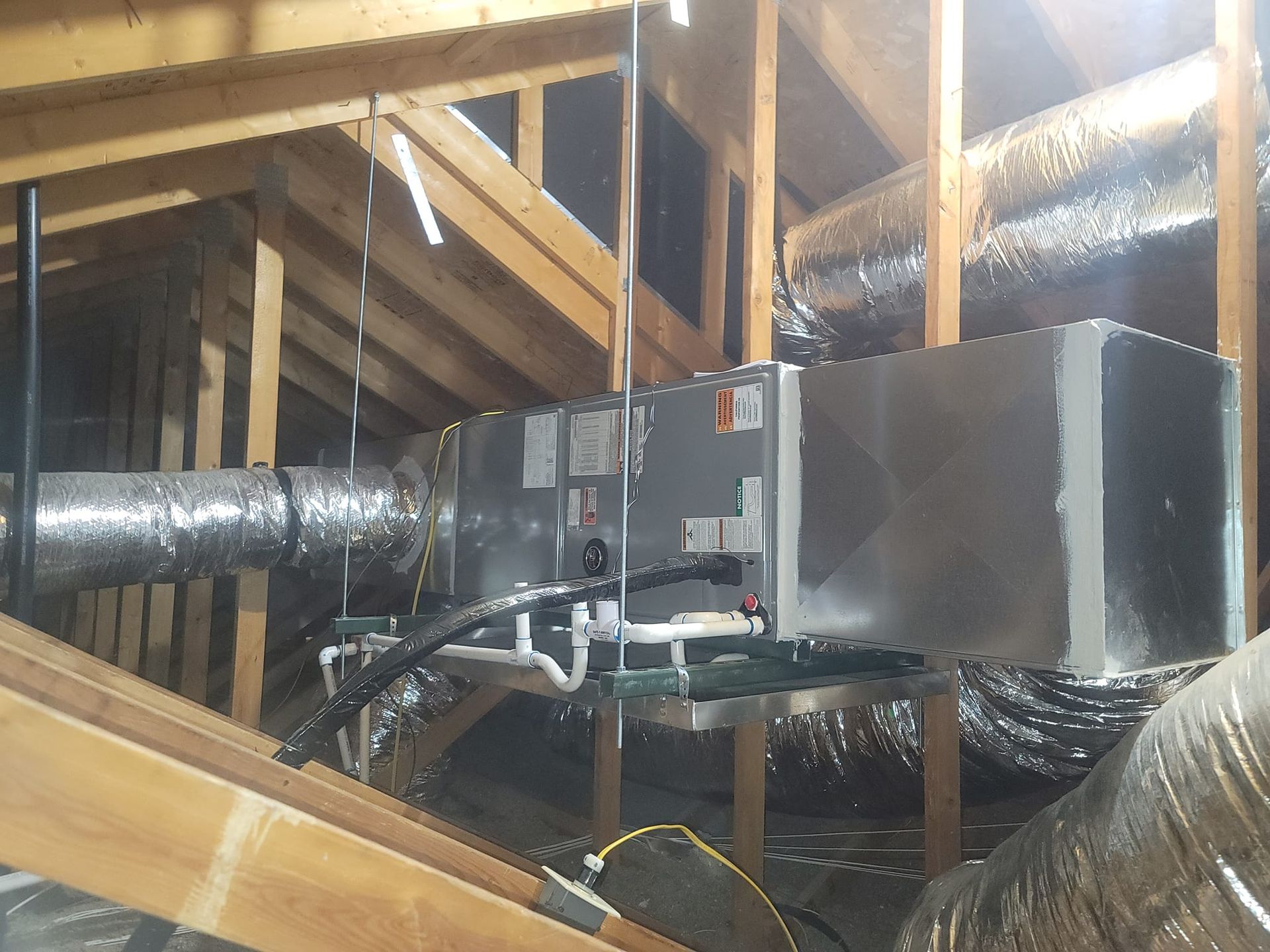 HVAC unit and ductwork installed in an attic. Aluminum and silver materials on wood framing.