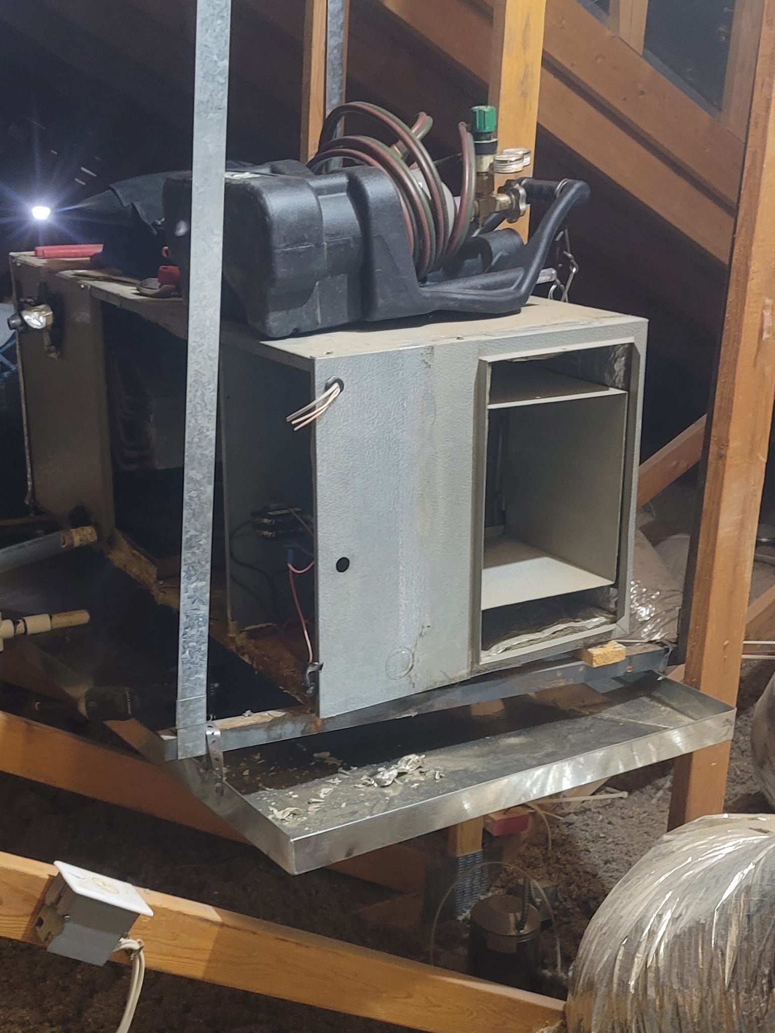An HVAC unit in an attic with ductwork, electrical components, and support beams.