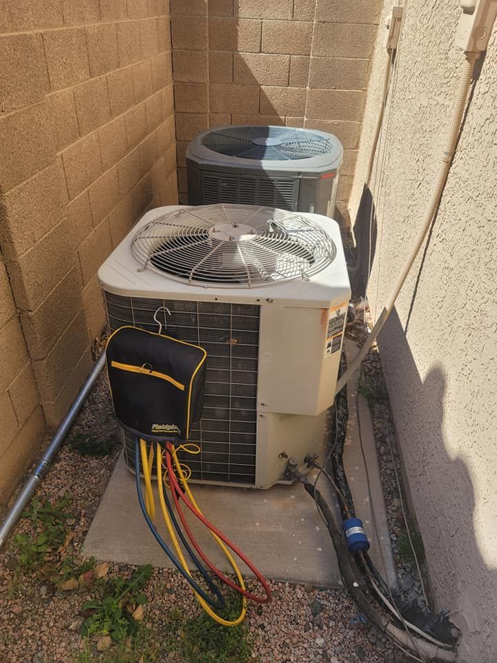 HVAC unit with gauges and hoses attached, situated between two walls on a concrete pad.
