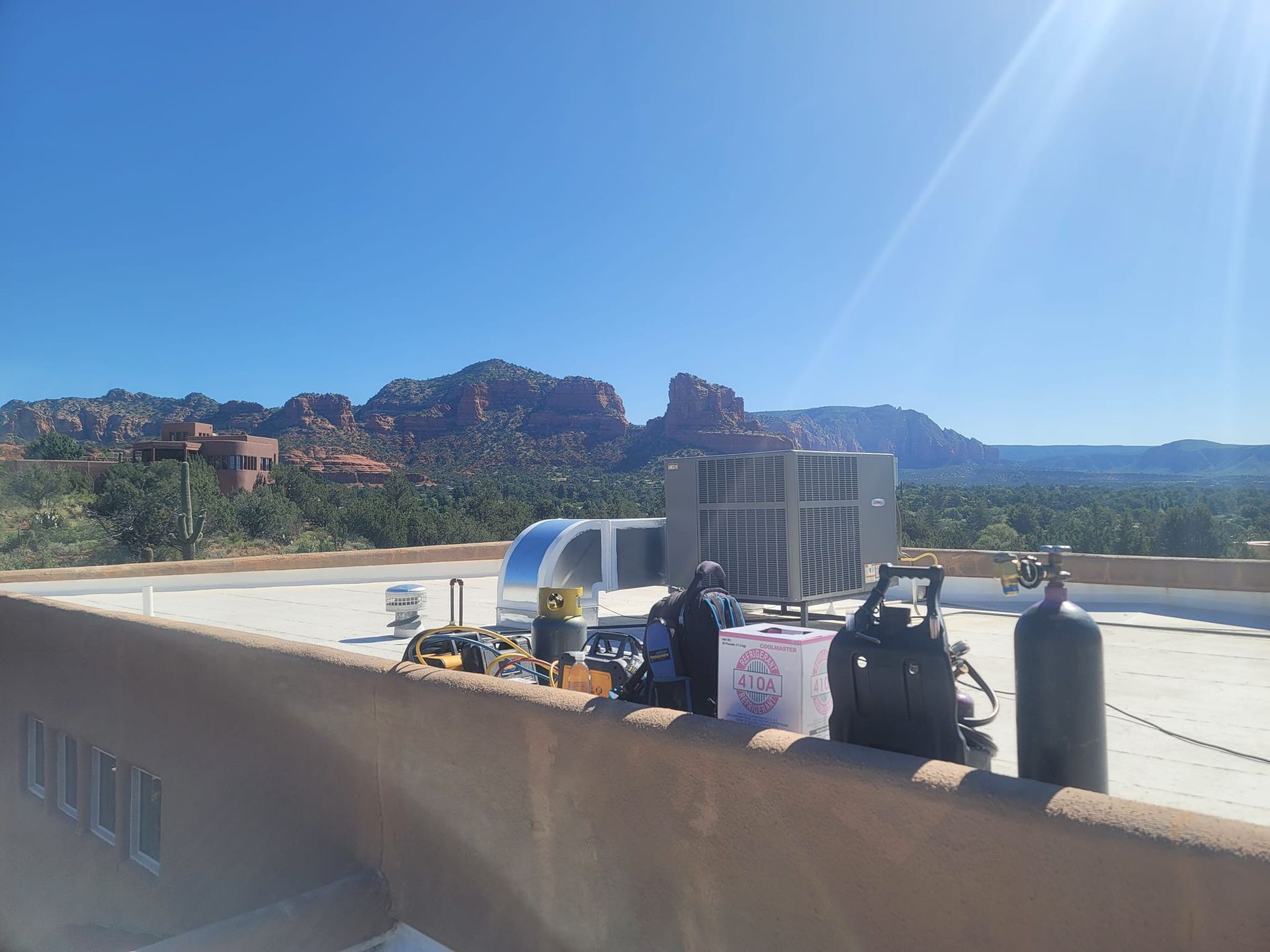 Rooftop with HVAC equipment and a person against a scenic desert mountain backdrop under a bright blue sky.