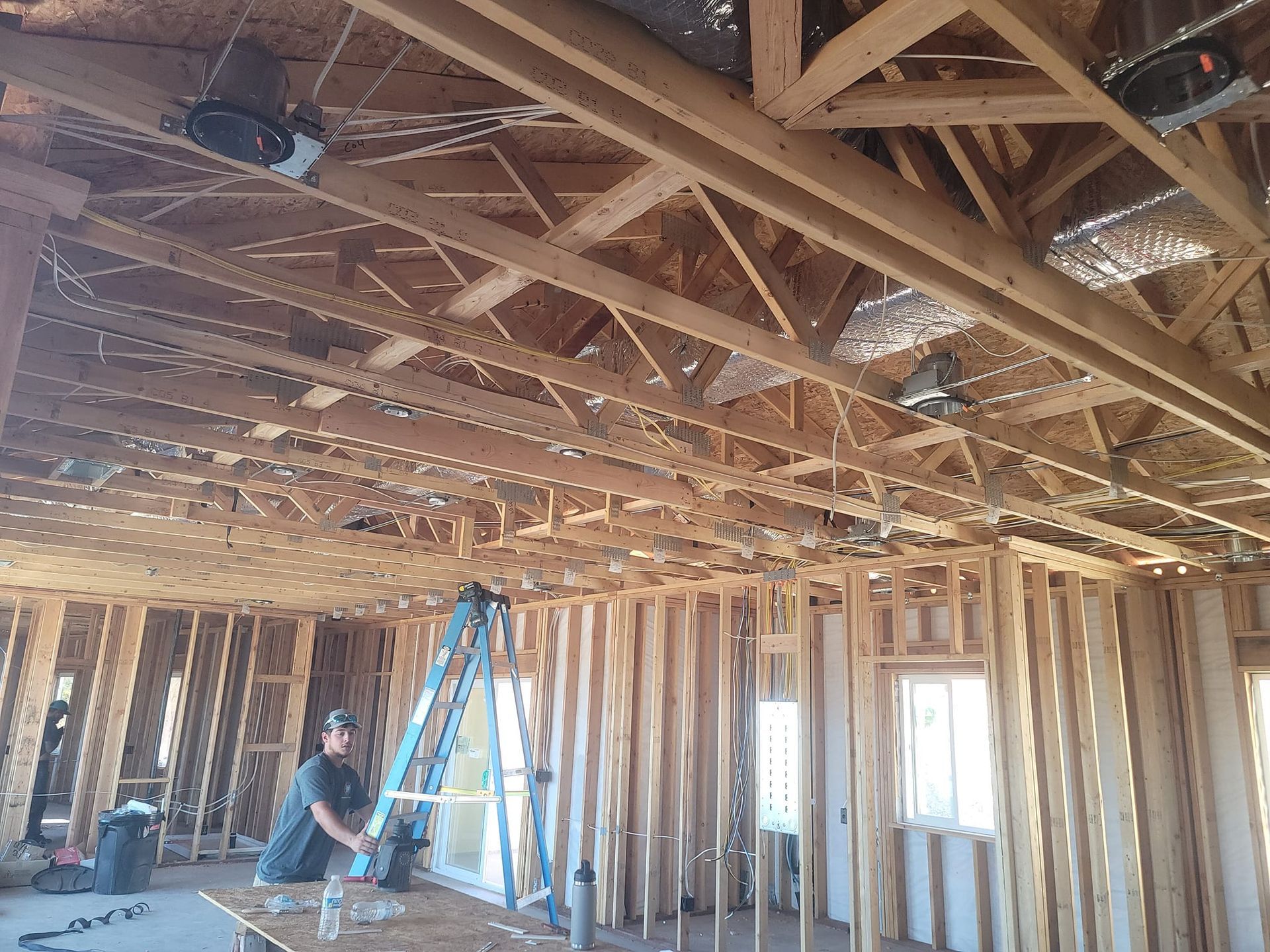 Construction site: Carpenter on a ladder, installing a window in a wood-framed building with exposed ceiling beams.