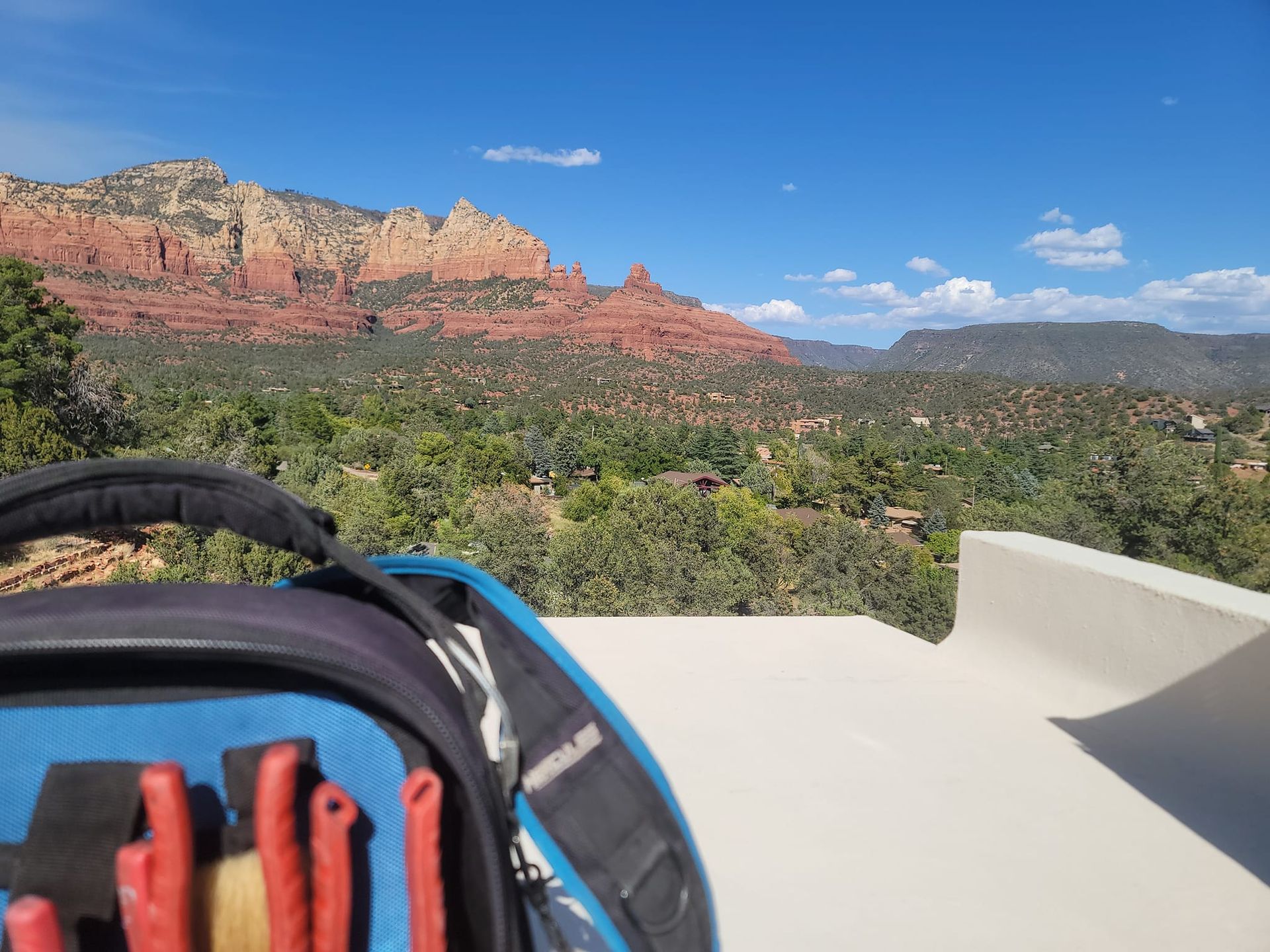 Tool bag on a white surface, red rock mountains and green landscape in the background under a blue sky.