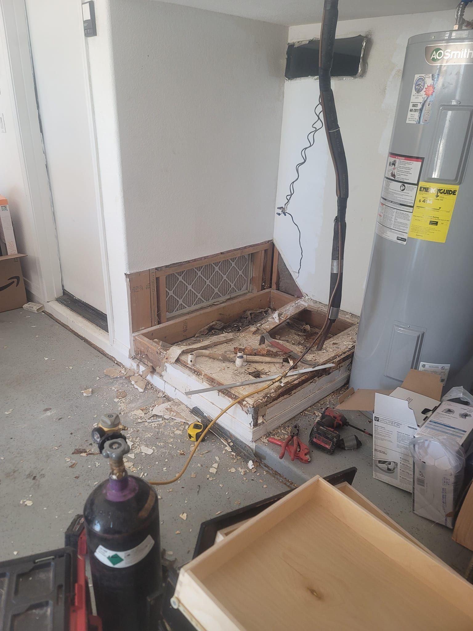 Garage with damaged wall and debris, tools, a water heater, and a welding tank.