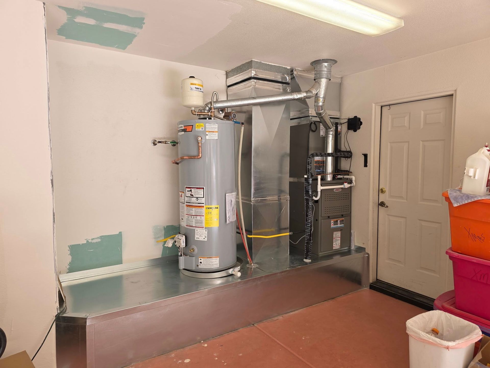 Water heater and HVAC system in a garage setting; white walls, metal components, and a closed door.