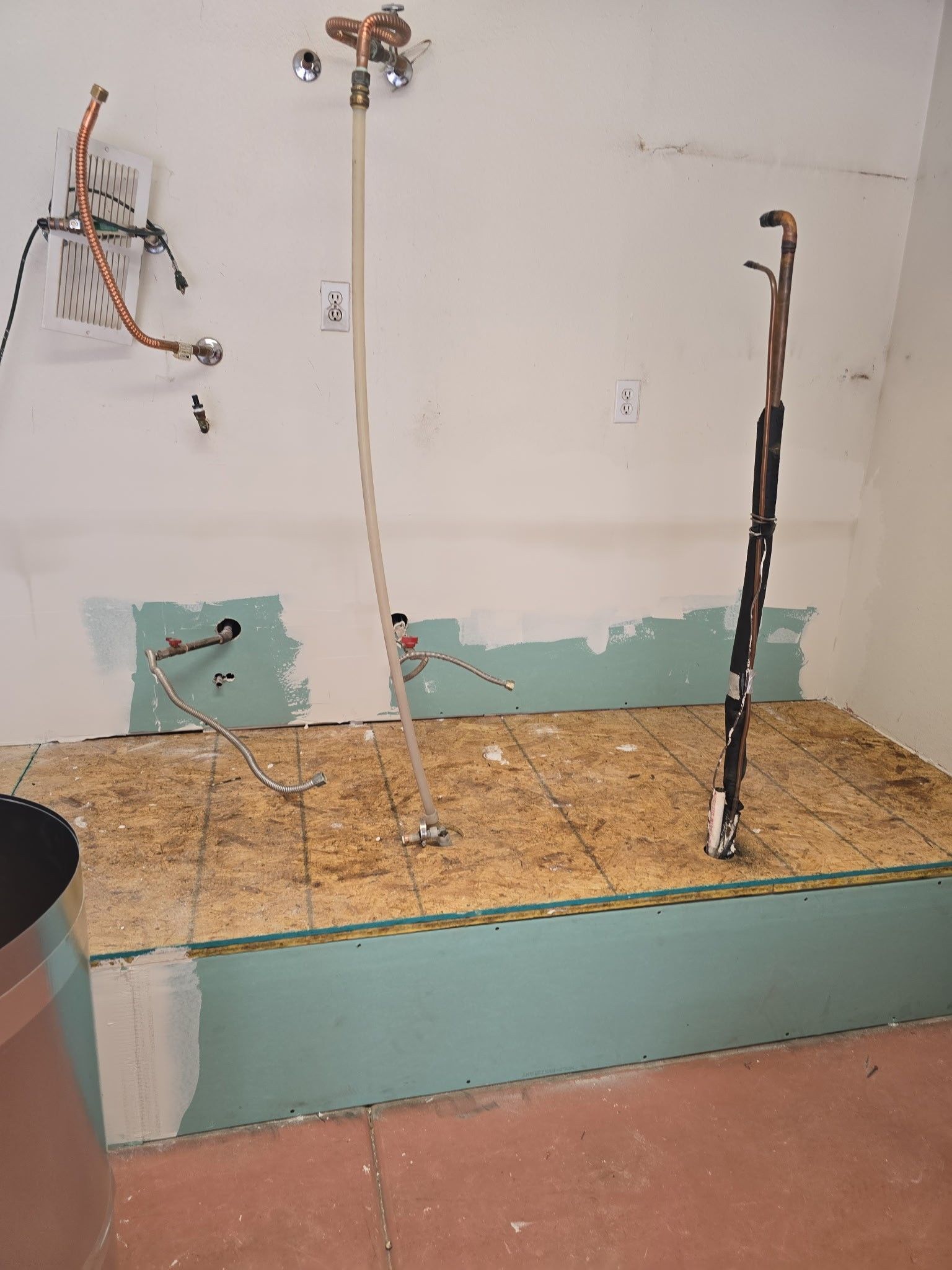 Bathroom renovation in progress; plumbing fixtures and electrical wiring exposed, unfinished drywall, wooden platform.
