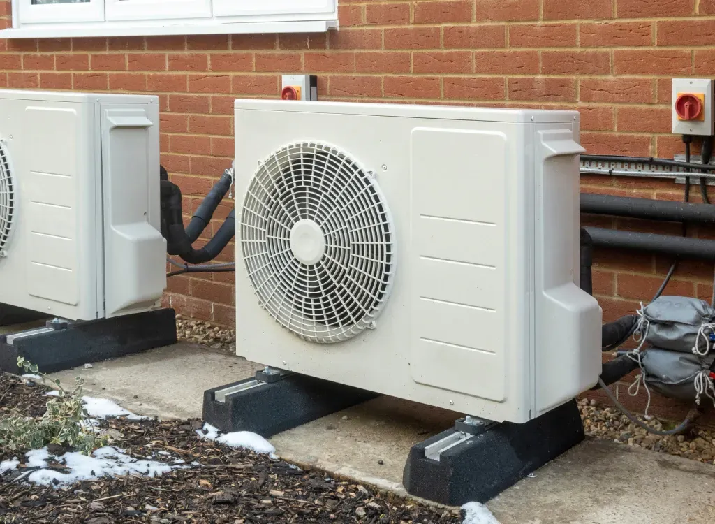 Two outdoor heat pump units on black bases next to a brick building.