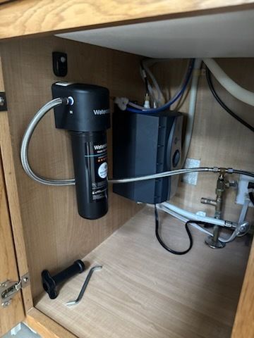 A water filter is sitting under a sink in a cabinet.