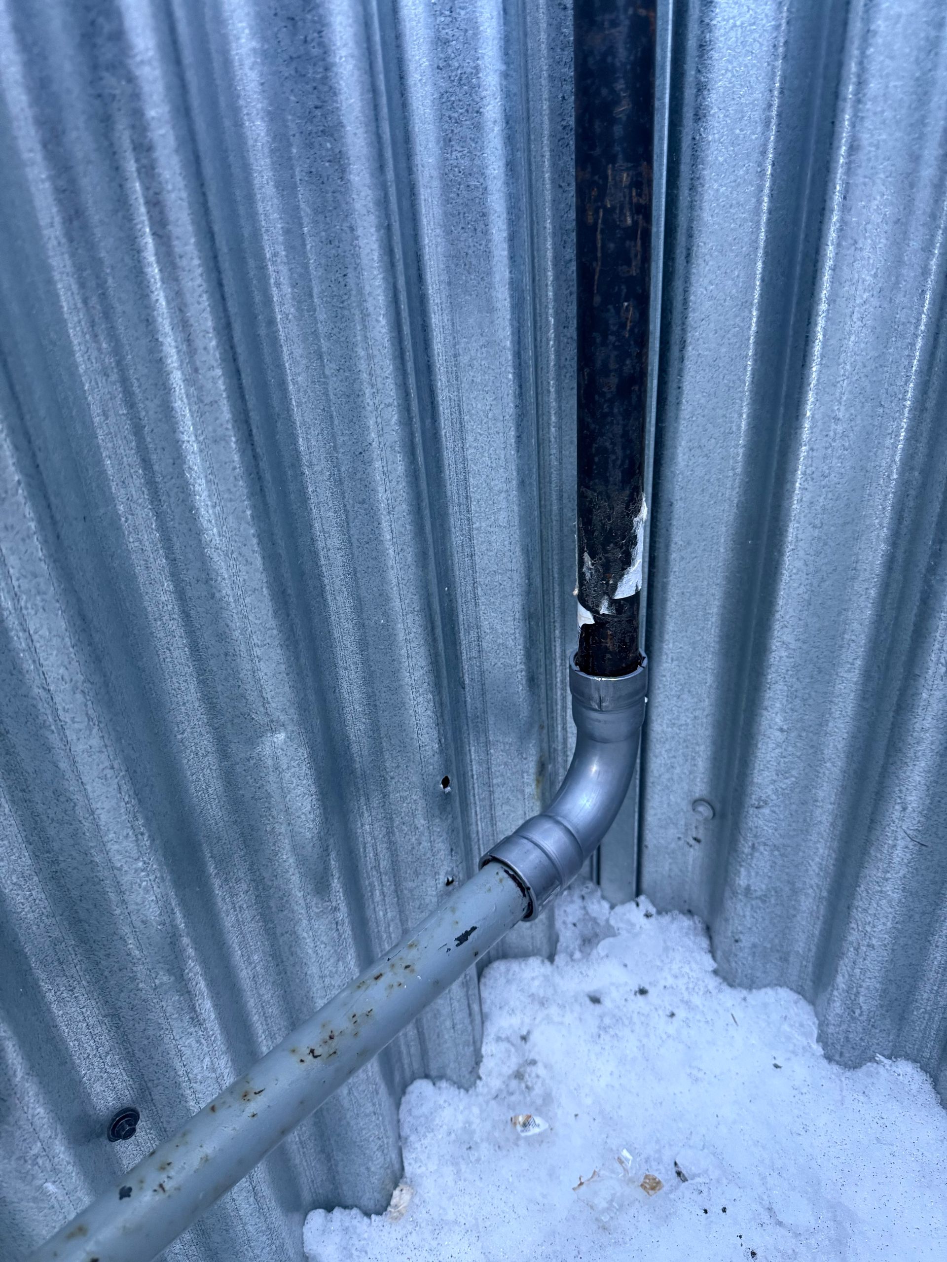 A pipe is coming out of a hole in a metal wall.