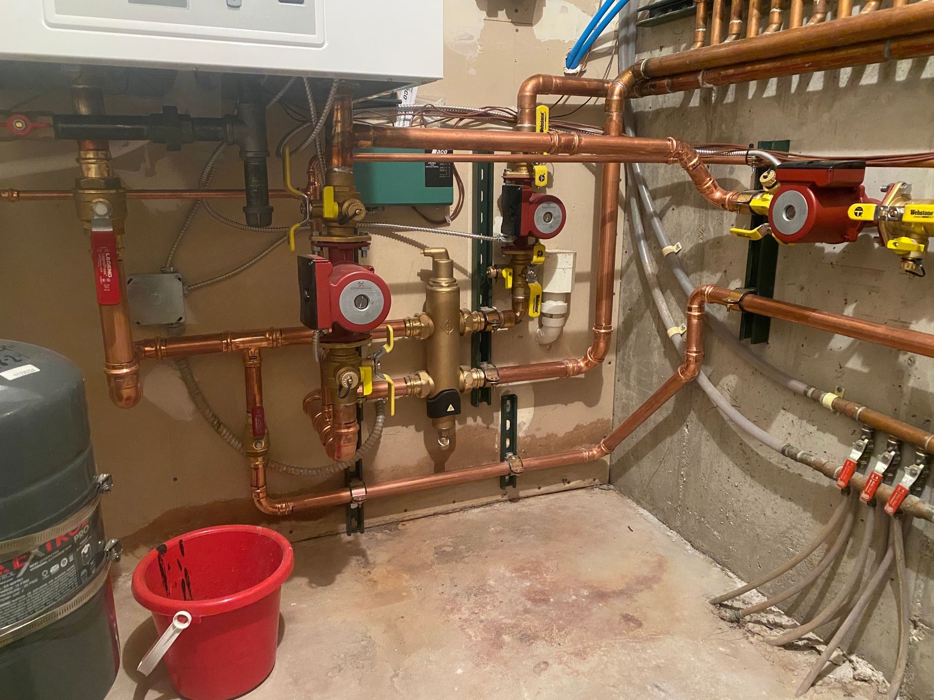 A room with a lot of pipes and a red bucket.