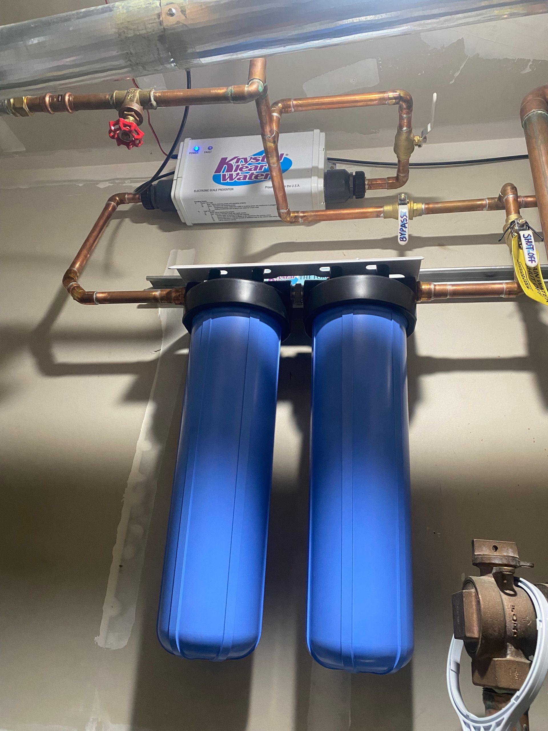 A blue water filter is hanging on a wall next to copper pipes.