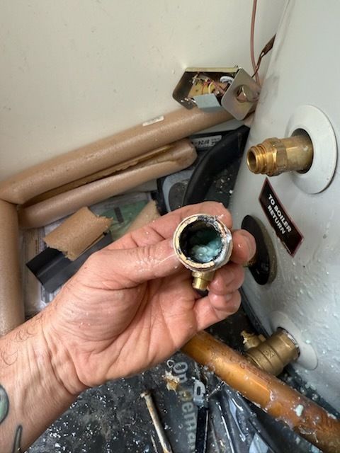 A person is holding a brass pipe in front of a water heater.