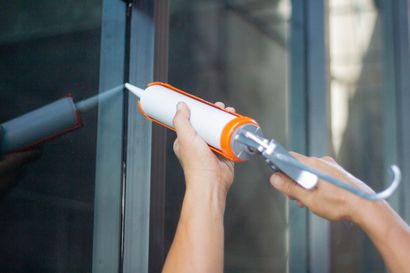 a person is applying silicone sealant to a window .