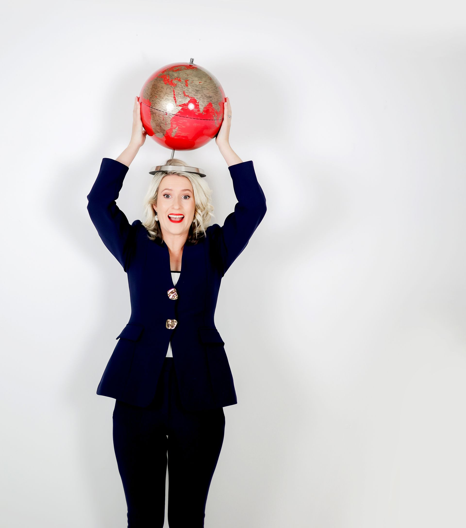 Woman in blue suit holding a red globe over her head against a white background.