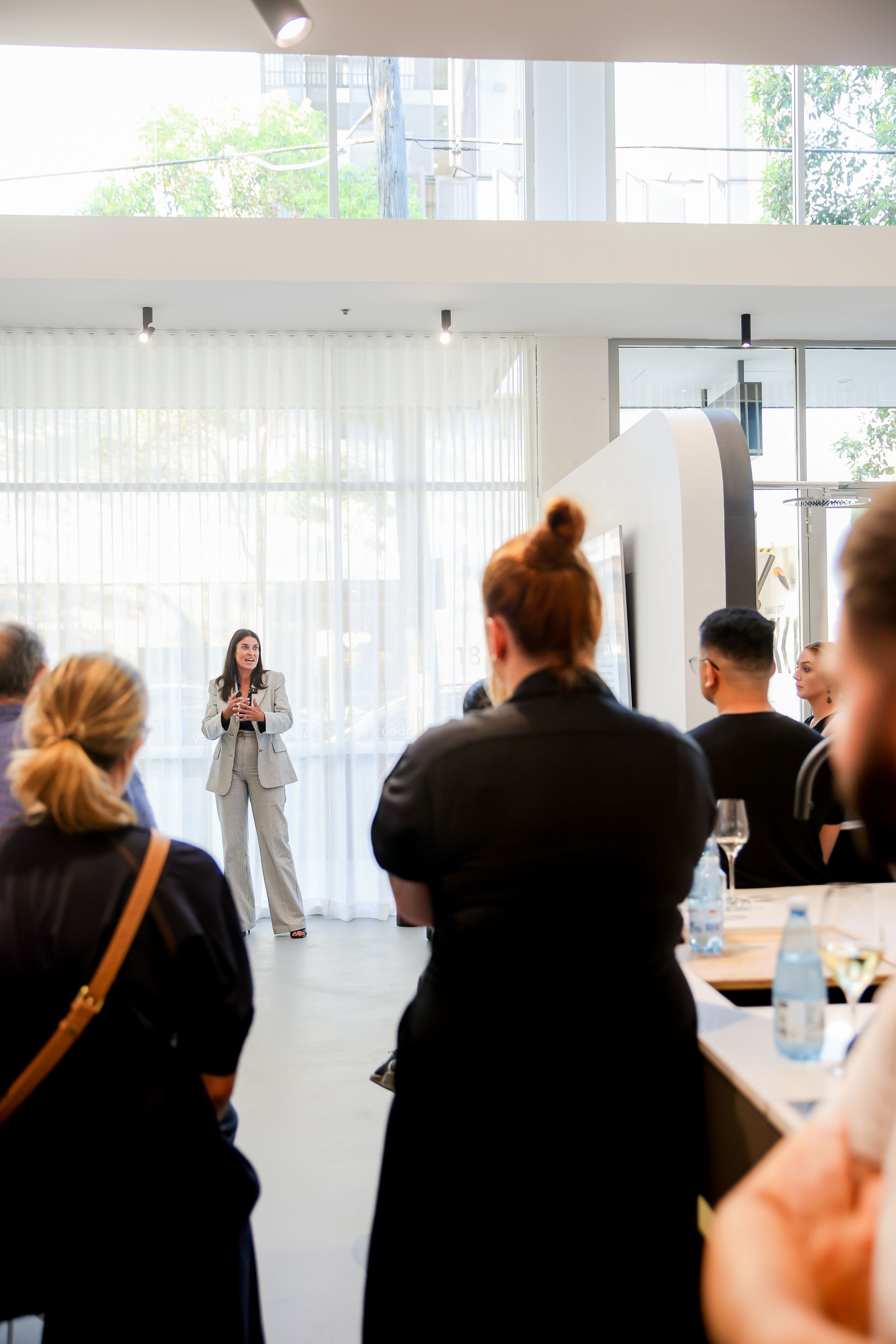Woman in suit speaks to a group; indoor event.