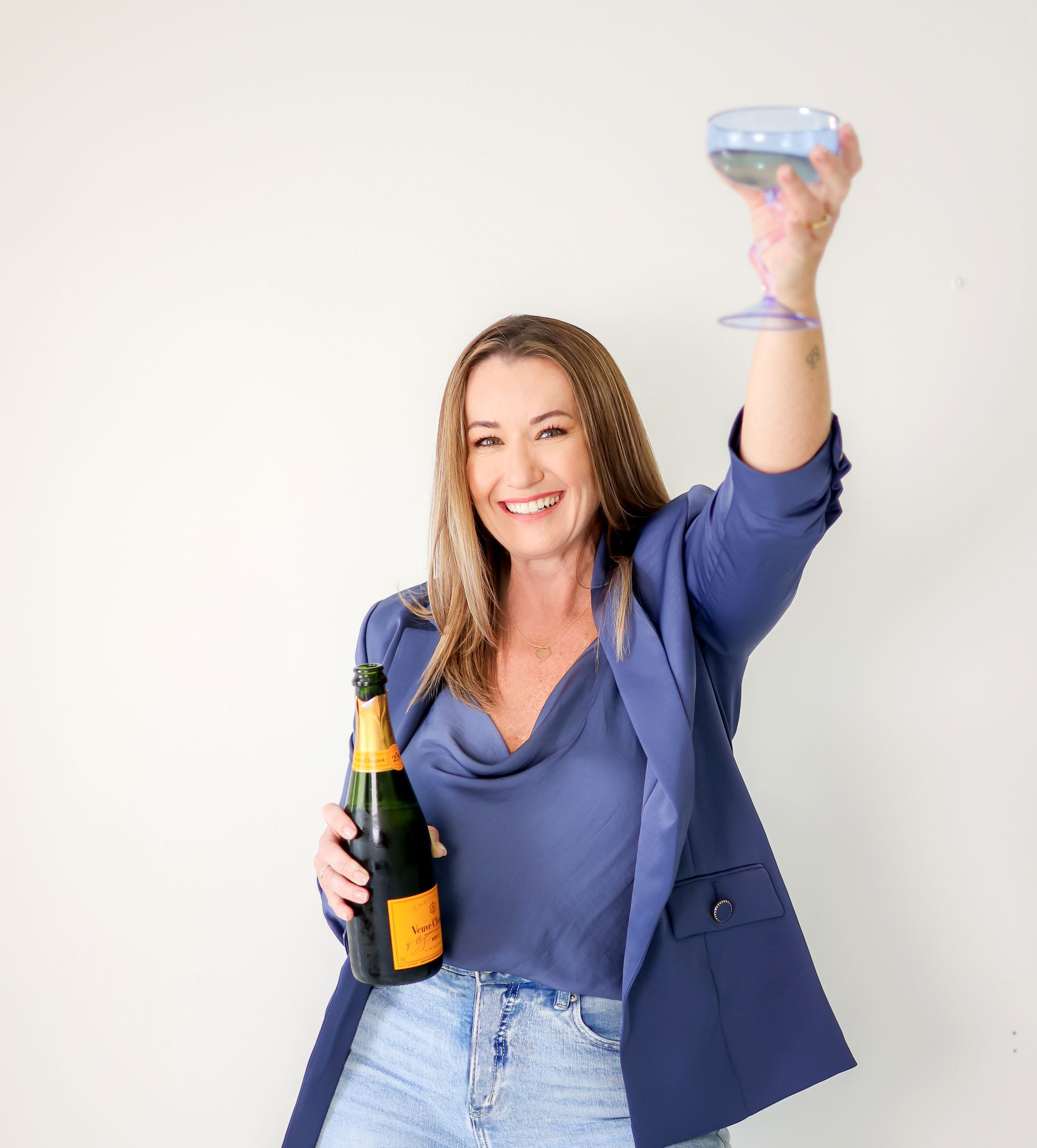Woman in blue blazer holding champagne bottle and glass, cheering.