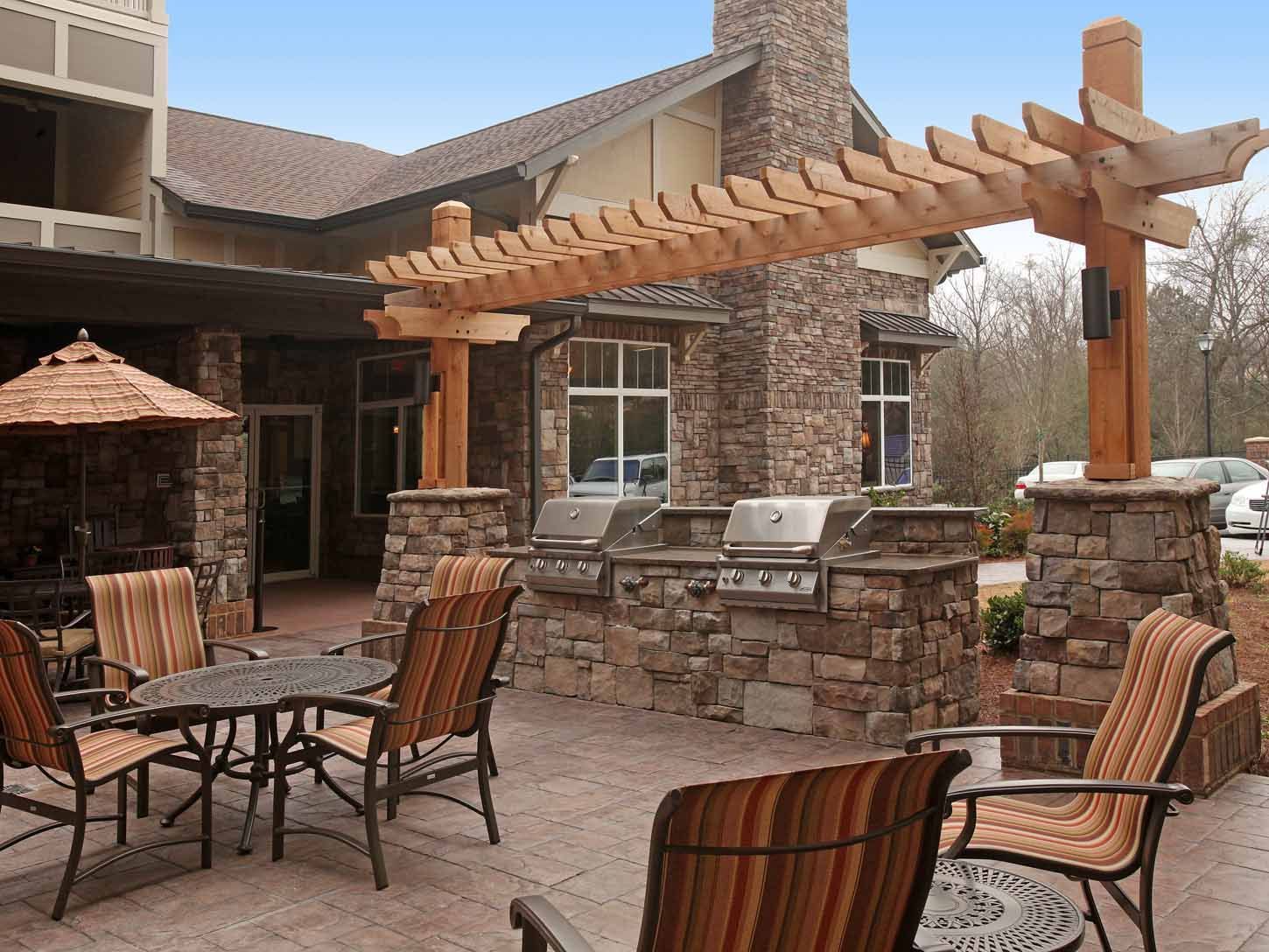 Outdoor communal grilling area with stone pillars, grills, and patio seating under a wooden pergola.