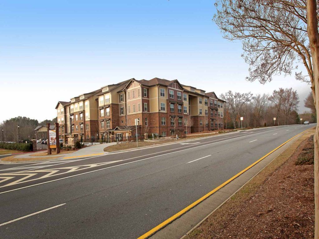 Exterior view of a multi-story apartment building along a road with landscaping.