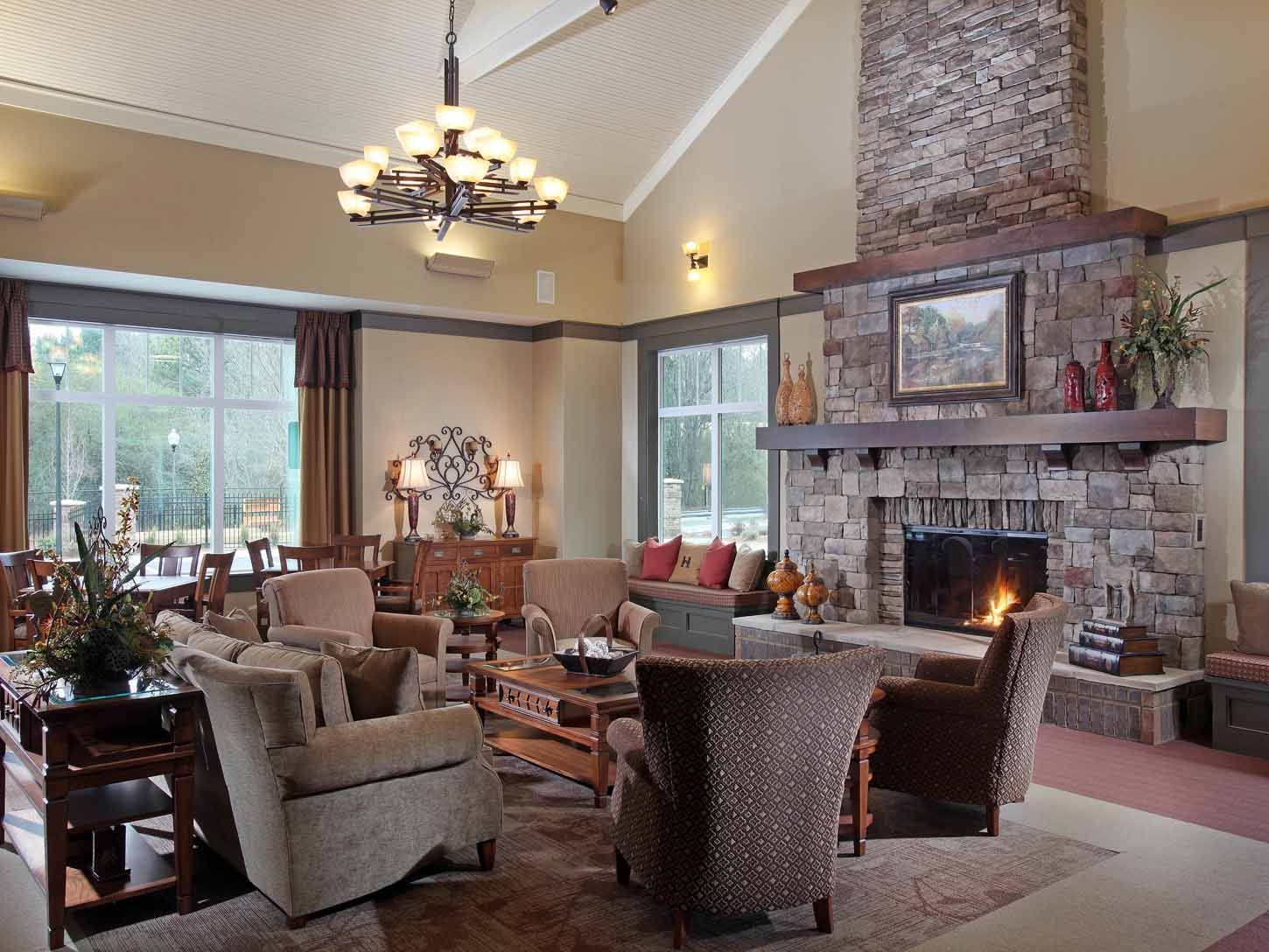 Community lounge with a stone fireplace, cushioned chairs, and large windows.