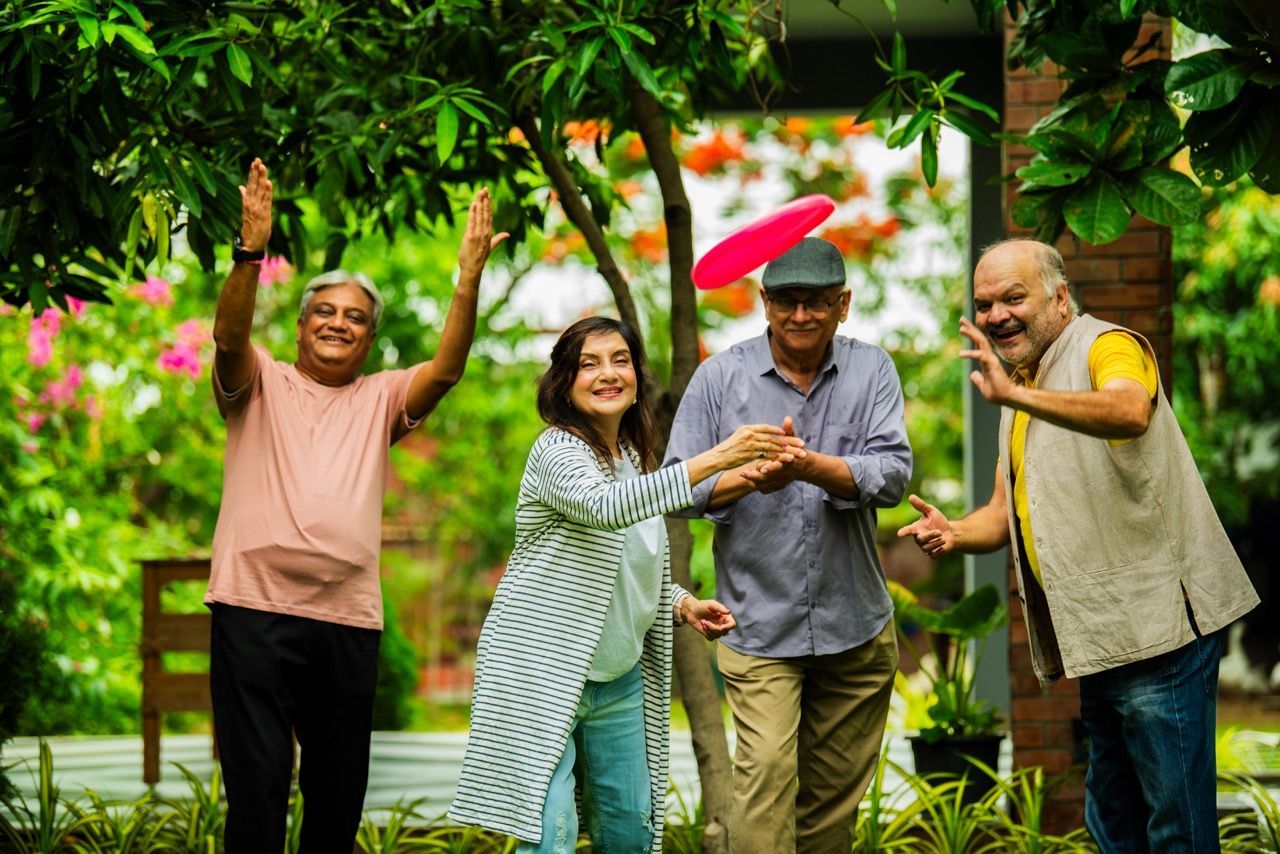 Group of four people playing with a frisbee in a garden; expressions of joy and reaching out.
