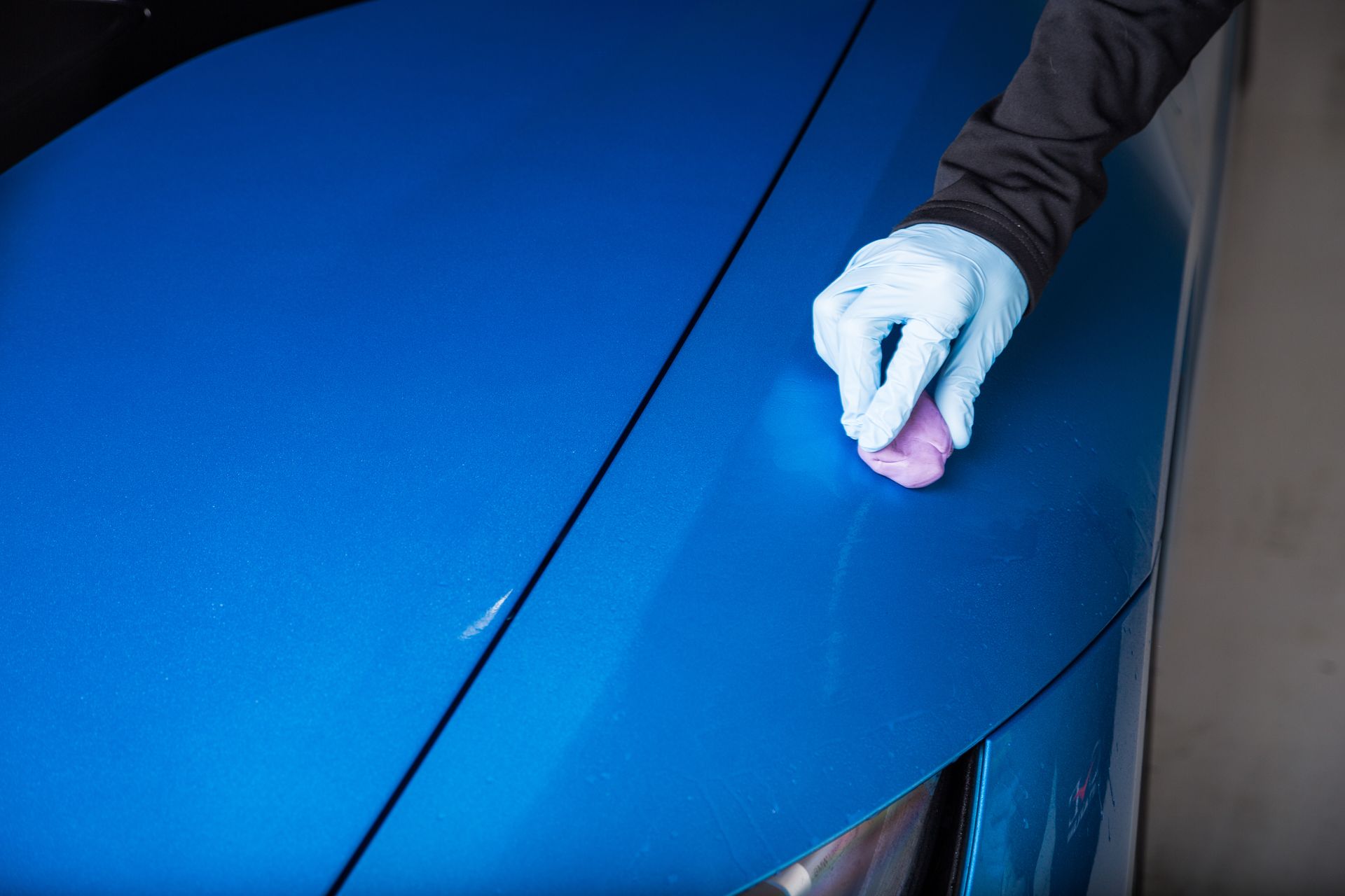 A person is polishing a blue car with a pink sponge