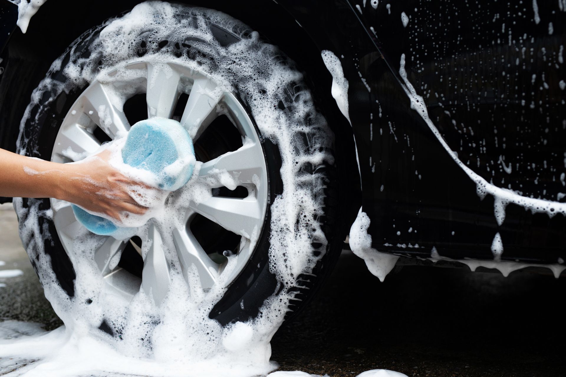 A person is washing a car wheel with a sponge.