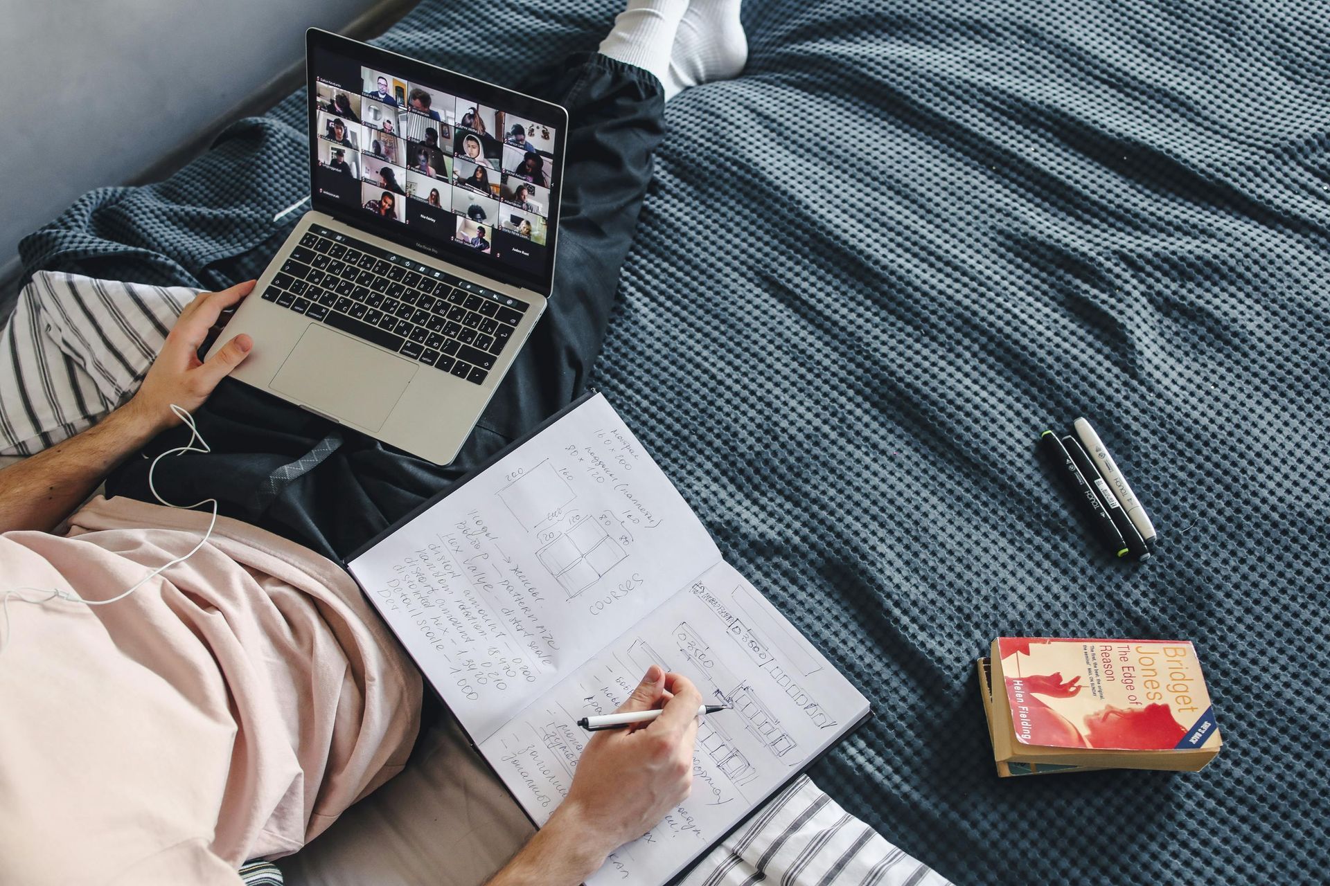A person is laying on a bed with a laptop and a notebook.