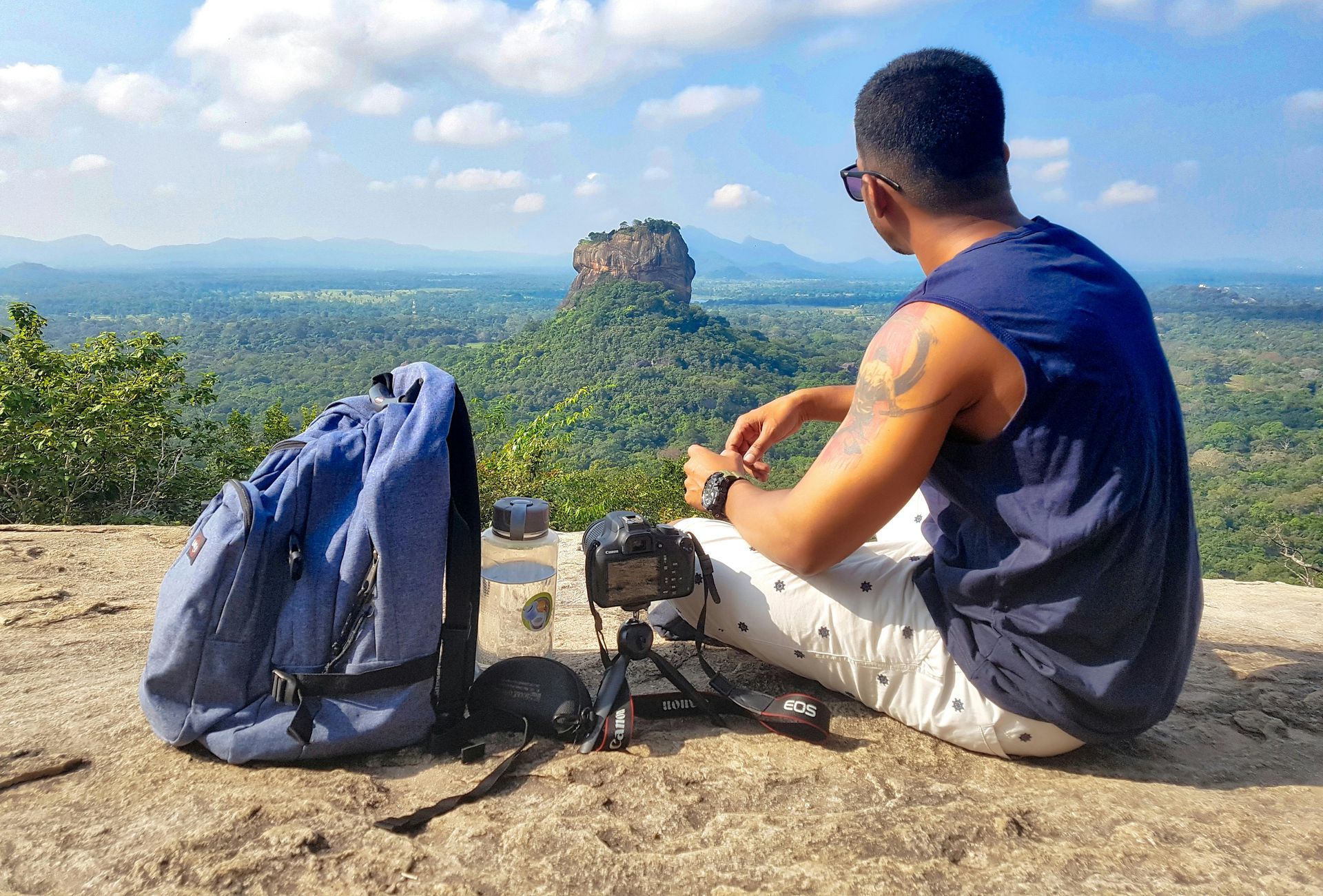 A man is sitting on top of a mountain with a backpack.