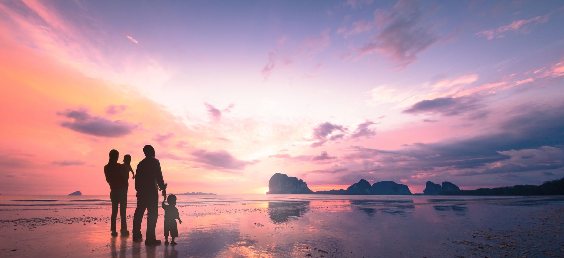 A family is standing on a beach at sunset.