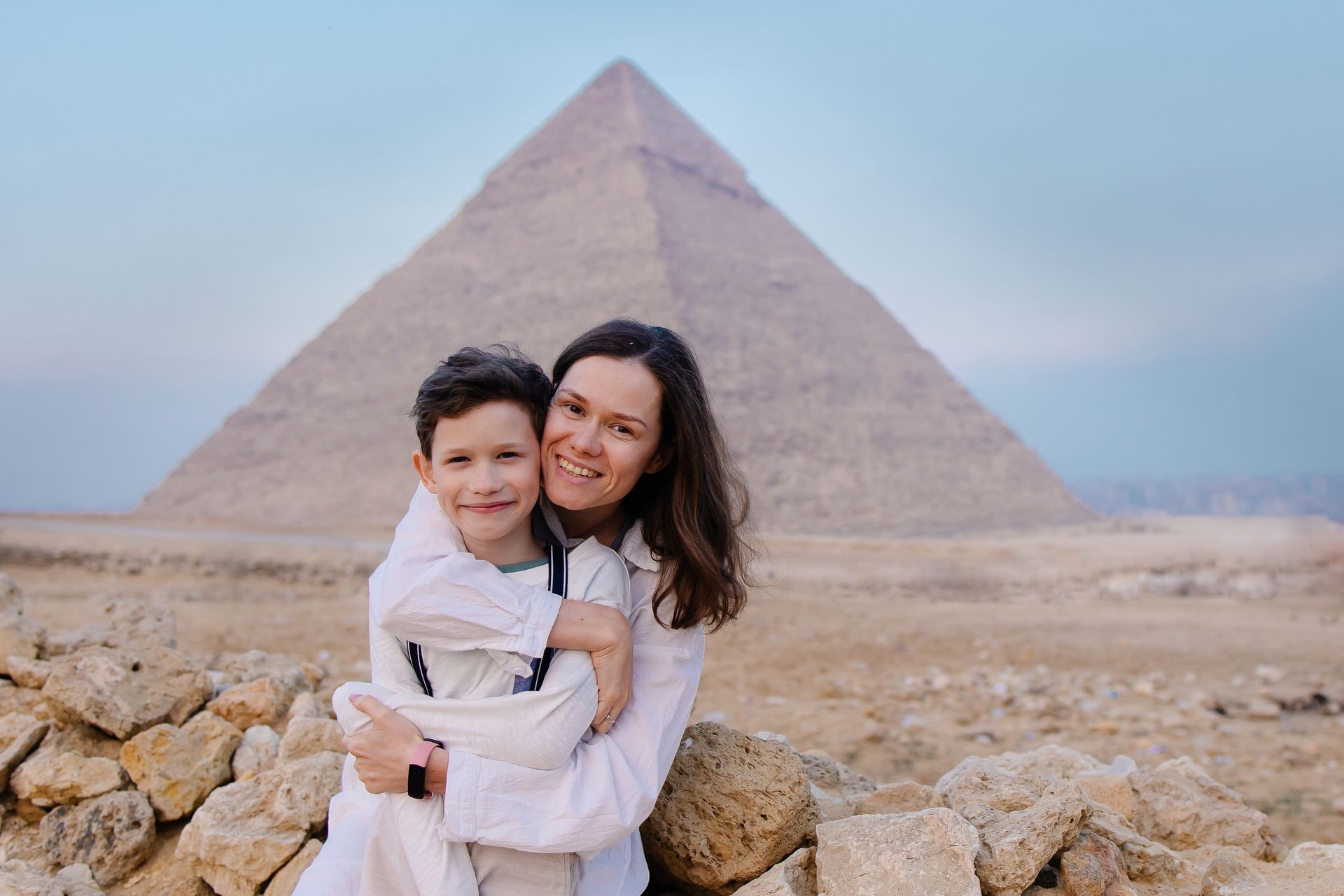 A woman is holding a child in front of a pyramid.