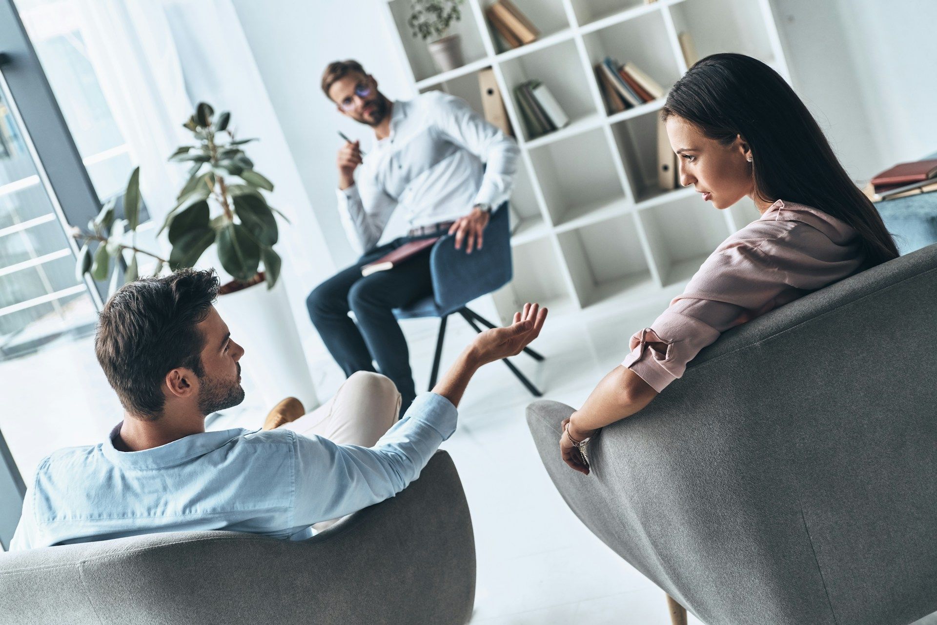 Couple in therapy, talking to a therapist in a modern office.