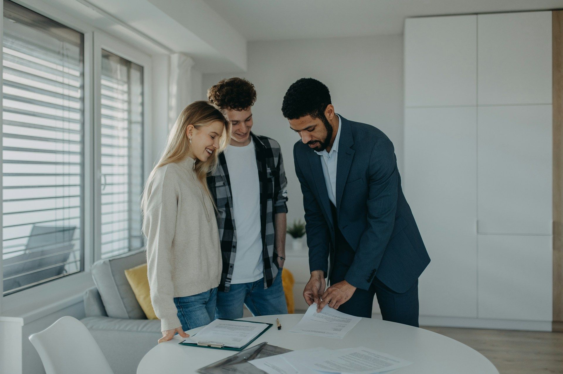 A real estate agent shows paperwork to a young couple in a bright living room.