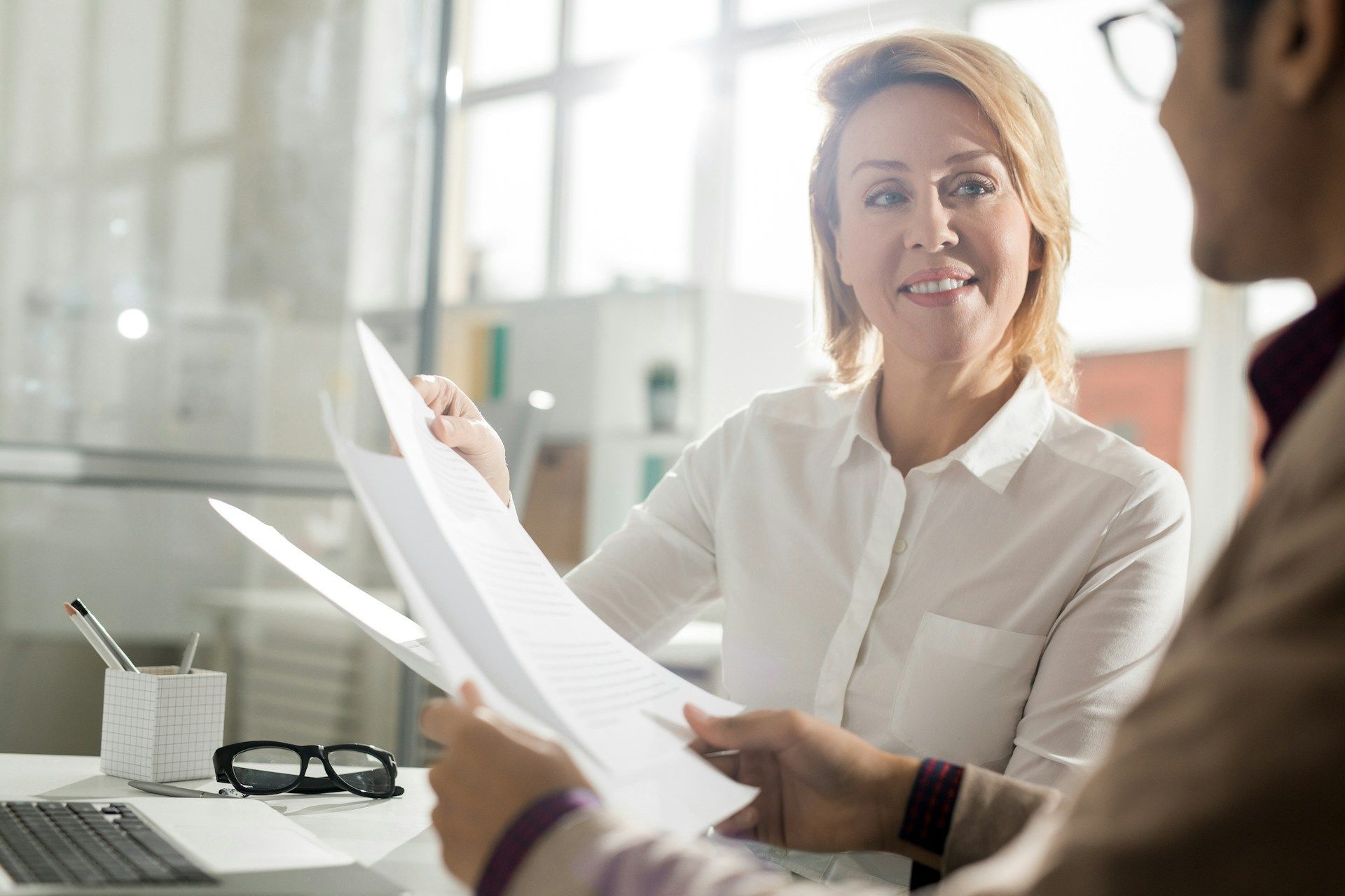 Woman and man in office setting reviewing papers; woman smiles.