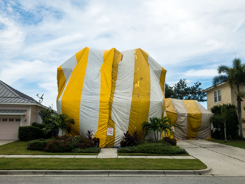 A close-up of a large yellow and white termite fumigation-tented home.