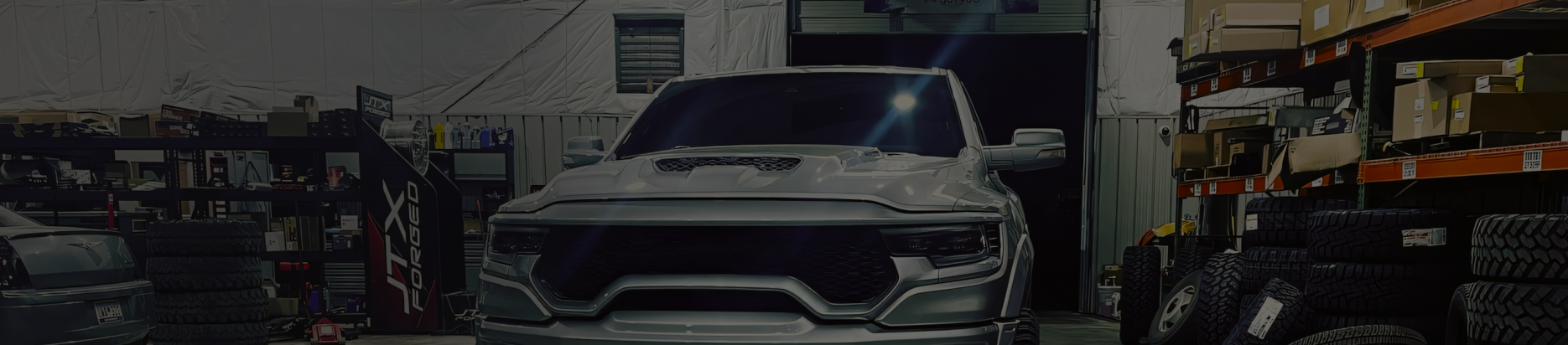 A modified truck inside a dimly lit garage. Shelves of tires are on both sides. The garage door is open | Marshside Motors