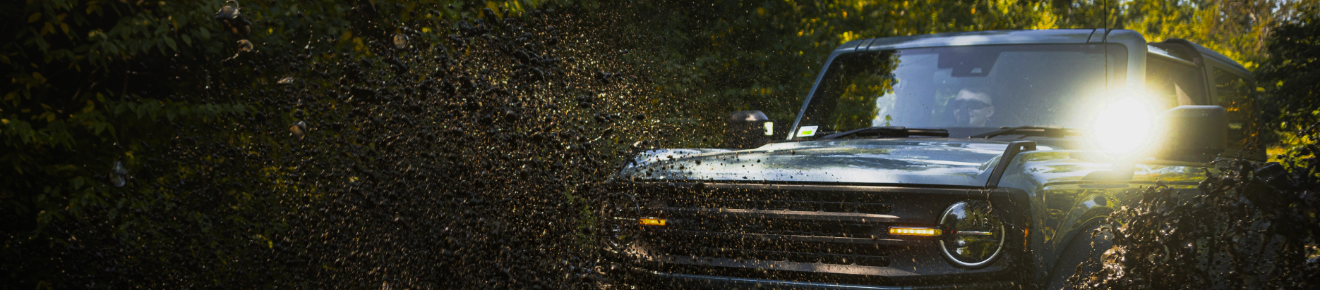 A black off-road vehicle drives through mud with its headlights on, in a forest setting | Marshside Motors